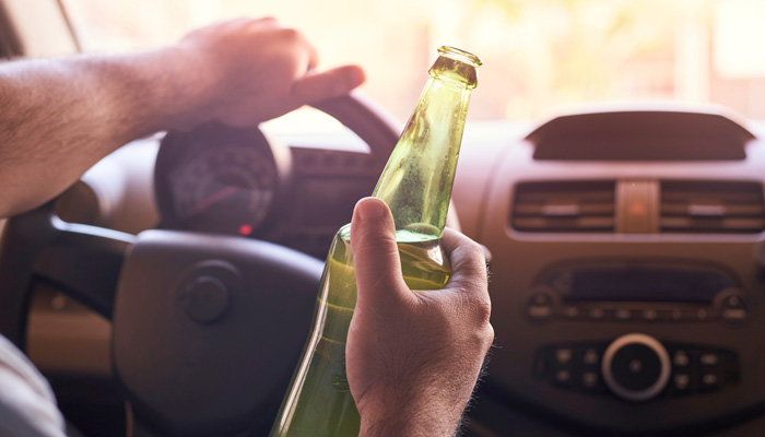 an unrecognizable man drinking beer while driving car
