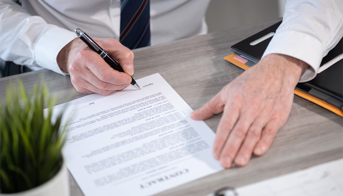 man signing contract sitting on desk