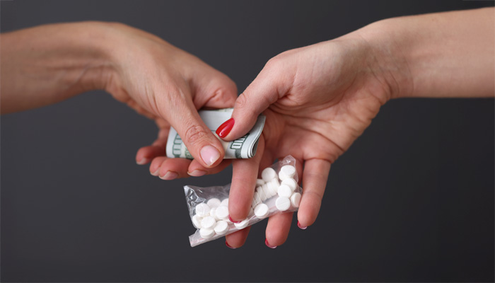 two people pass pills and money to each other