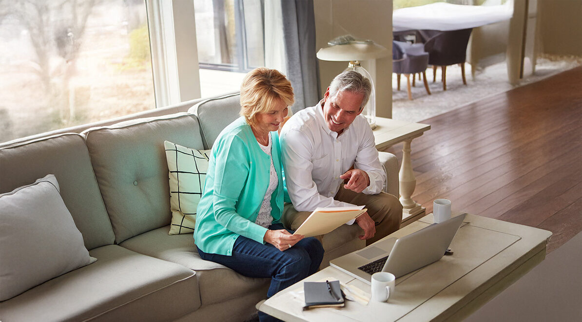 senior couple sitting on the couch with documents and a laptop