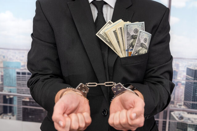 young male businessman in a classic suit and tie holds his hands in handcuffs. The concept of a man in handcuffs.