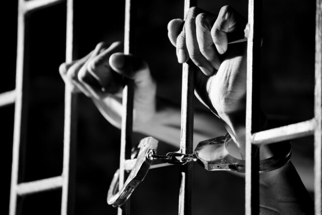 hand on jail cell bars handcuffs
